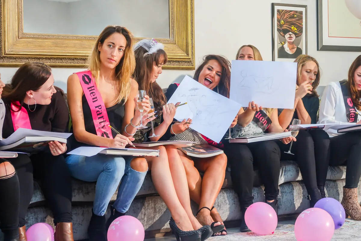 Hens with sketch pads and sashes on a sofa at a life drawing class
