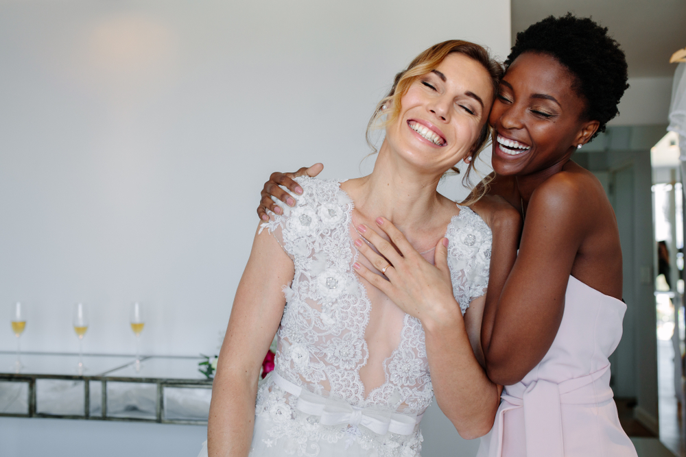 Gorgeous bride in wedding gown having fun with bridesmaid in hotel room.